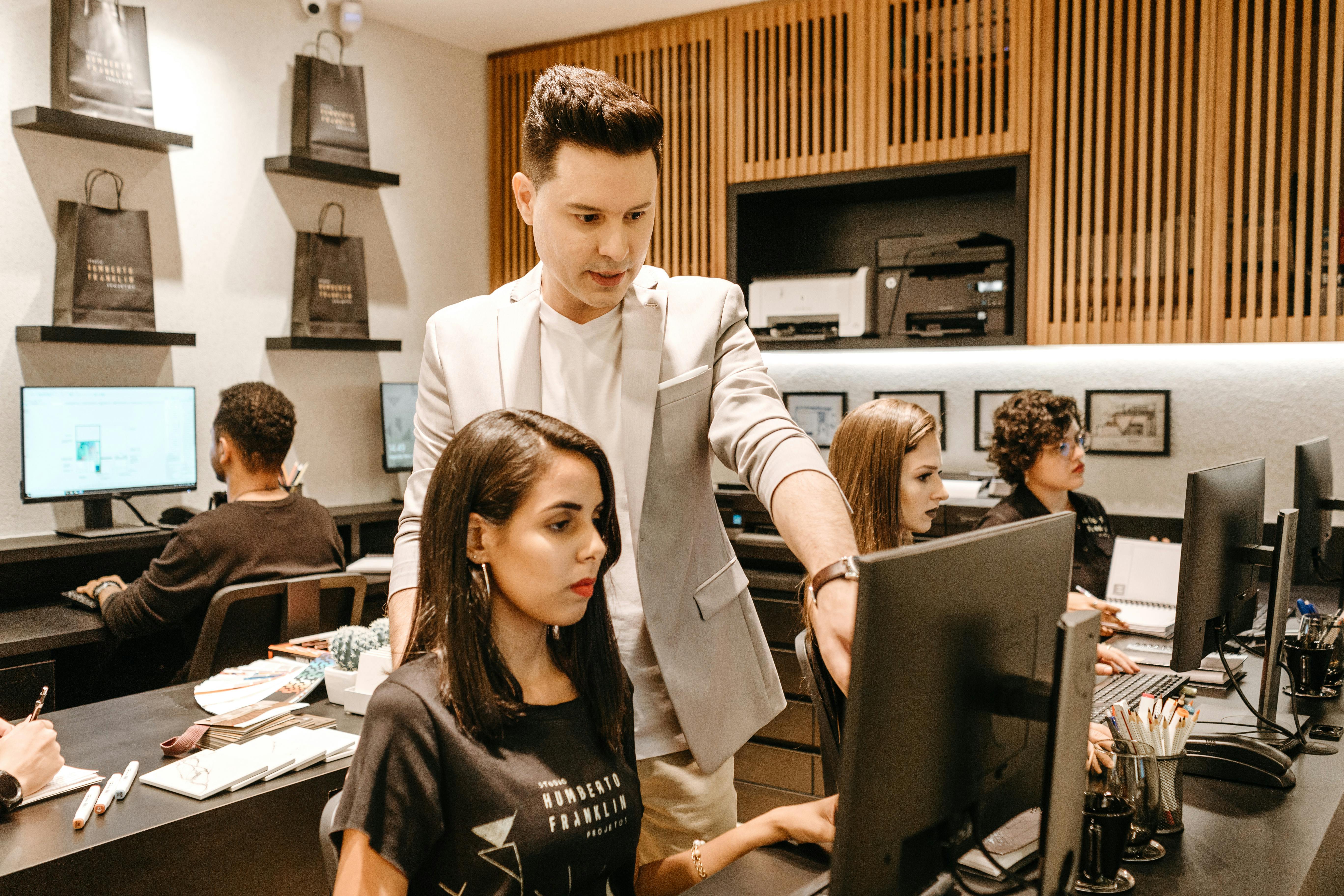 An image of a male manager helping a female programmer on the team. He is pointing at the screen.